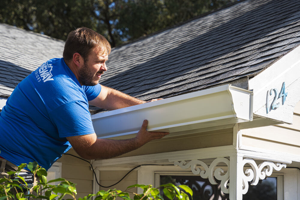 professional in blue shirt installing gutter on home